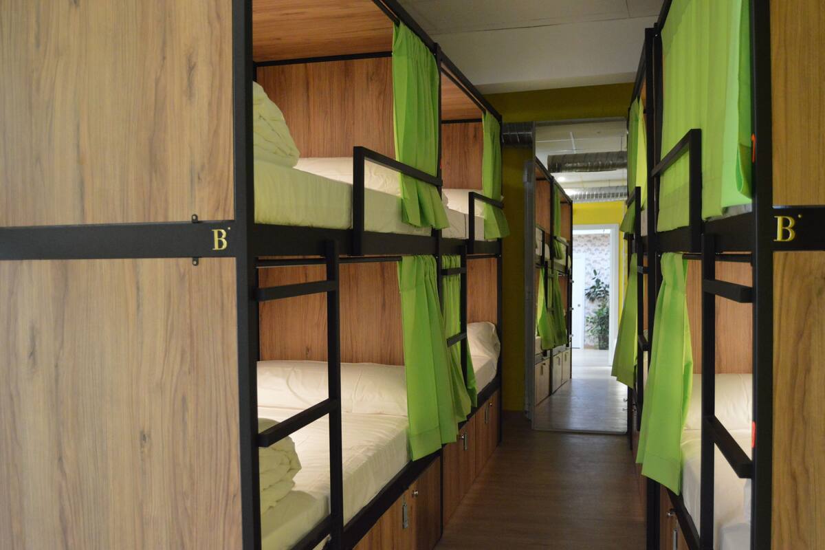 A corridor with bunk beds, each with a green curtain.