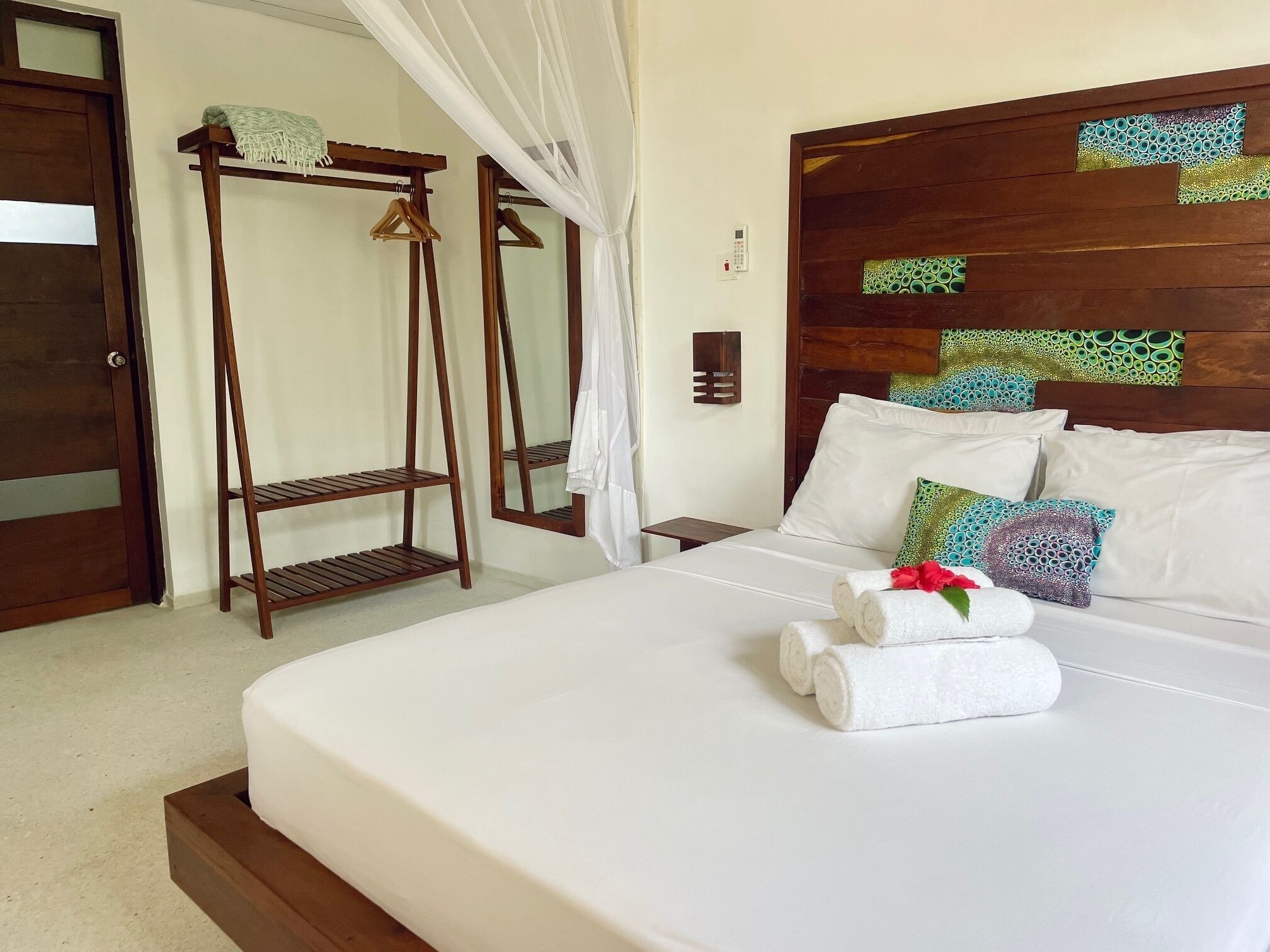 Una cama bien hecha con sábanas blancas, un cabecero de madera con paneles decorativos y una mesita de noche con una lámpara.