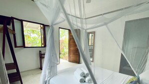 A bedroom with a bed, a wooden ladder, a window with a view of greenery, and a mosquito net. - Gaia Villas (Nungwi)