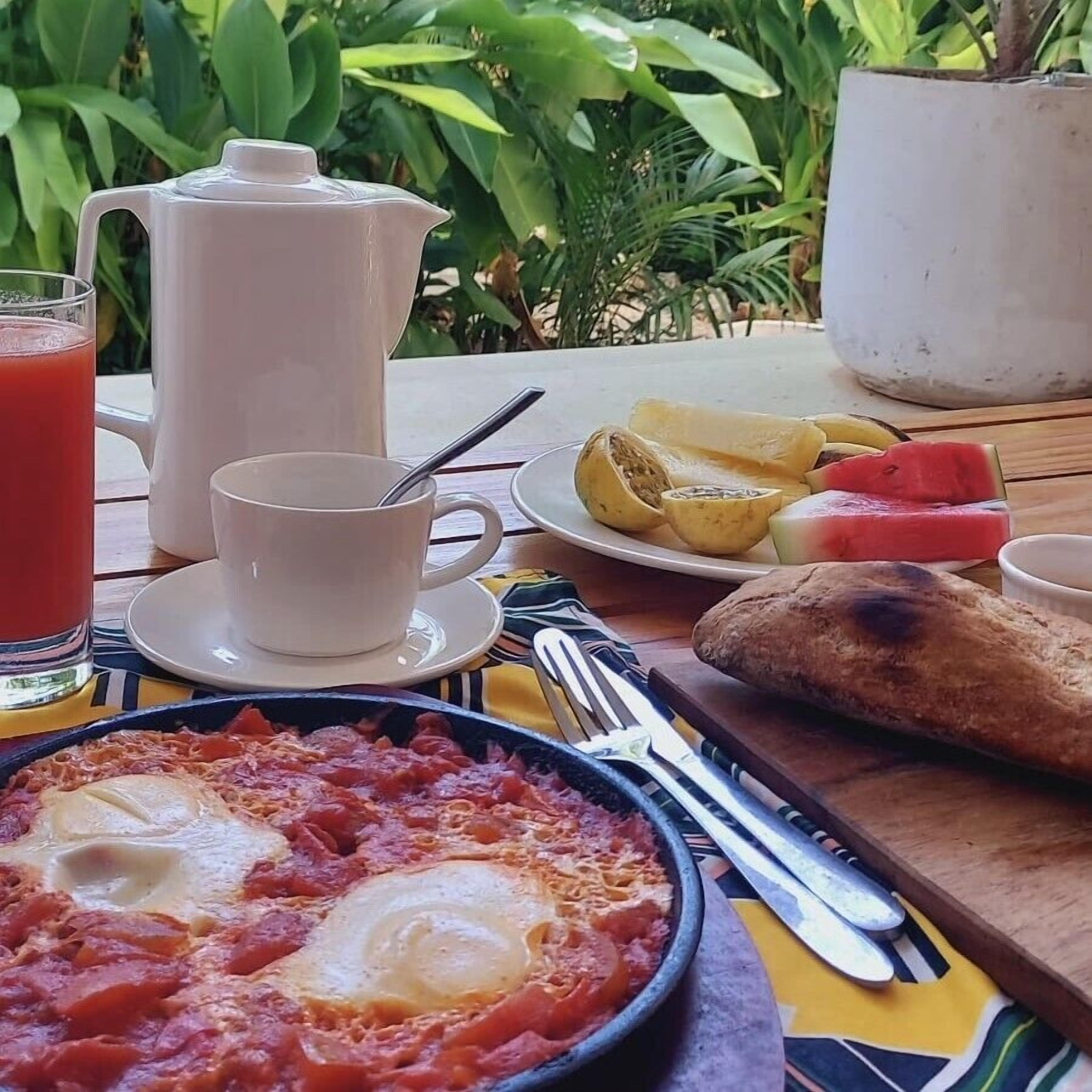 Une table de petit-déjeuner avec une assiette d’œufs, un pichet, une tasse et un verre de jus d’orange.