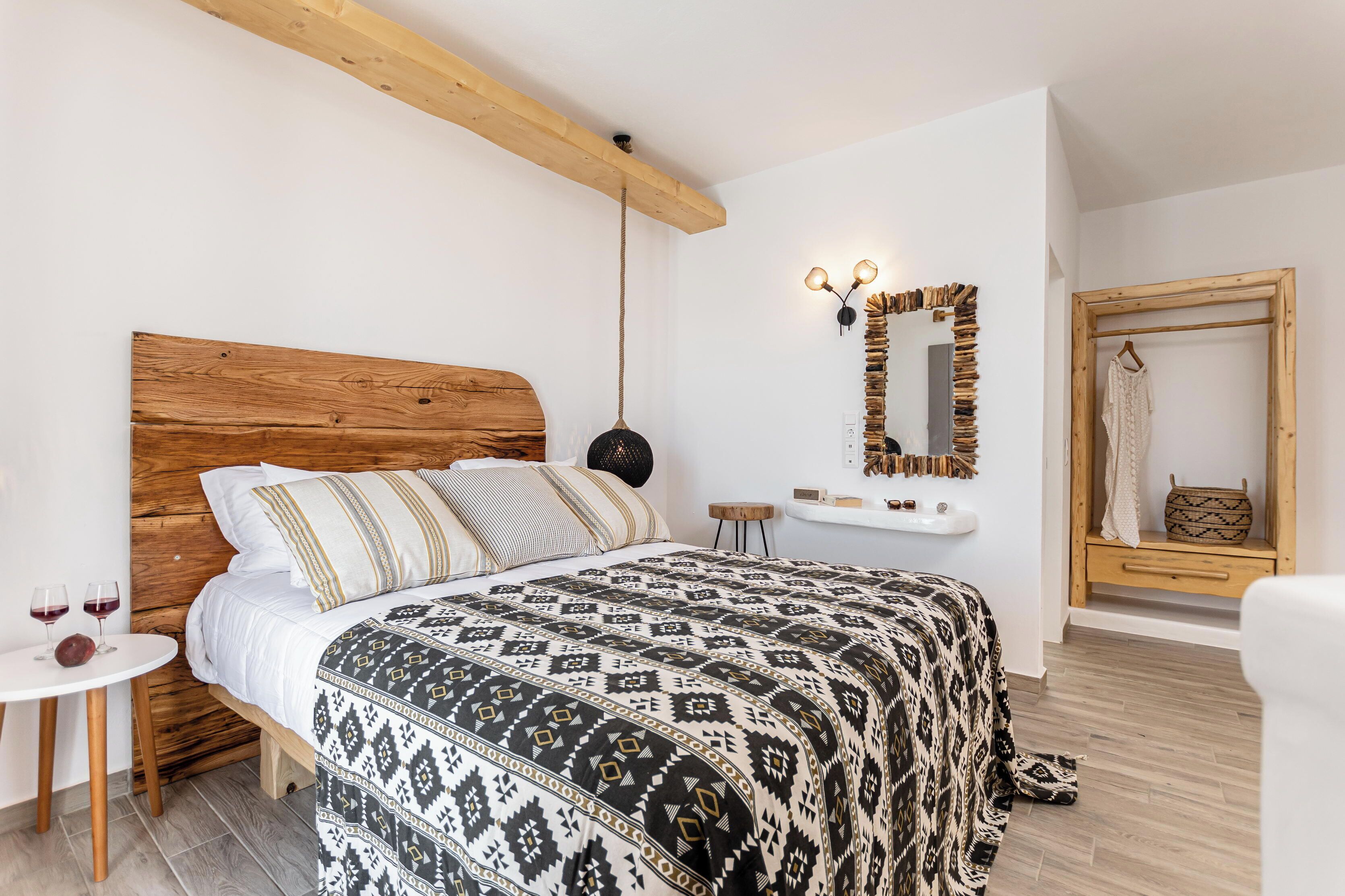 A bedroom with a wooden headboard, a patterned bedspread, a small bedside table with wine glasses, and a mirror with a unique frame.