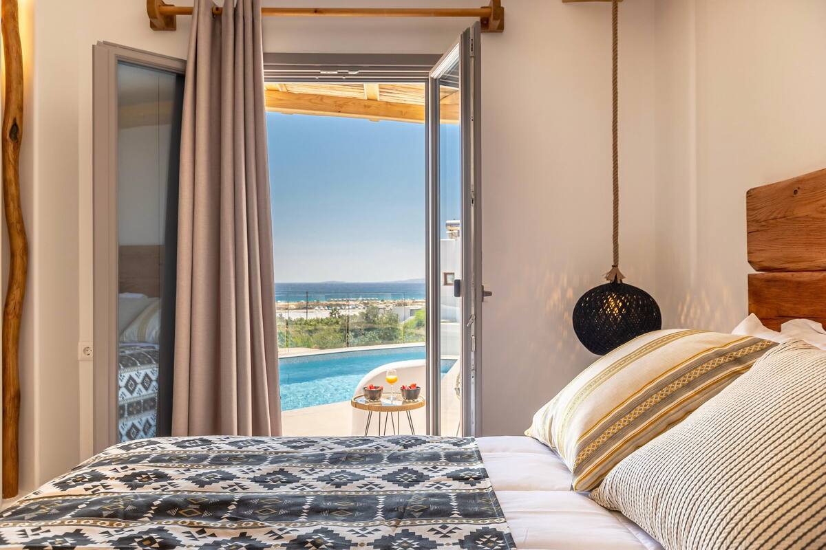 A bedroom with a bed, a view of a swimming pool, and a balcony with a table and chairs.