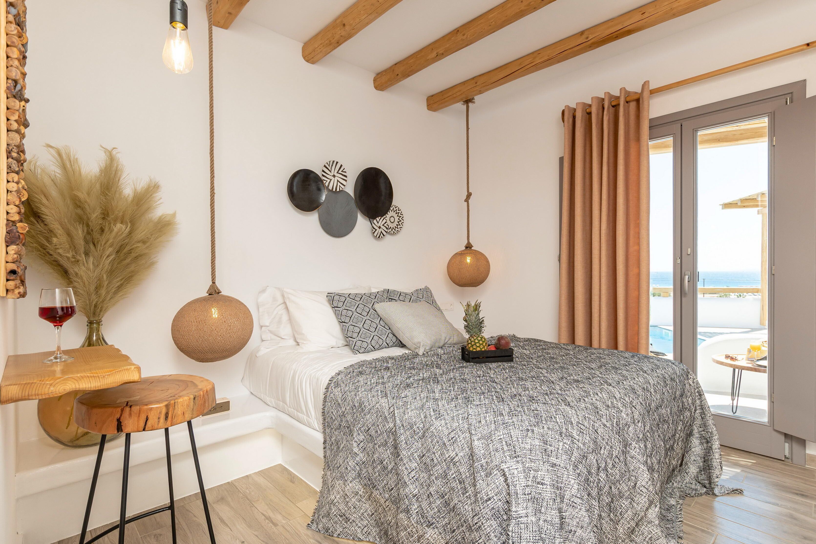A bedroom with a bed, a wooden table with a glass of red wine, and a view of the sea through a sliding door.
