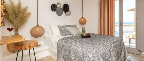 A bedroom with a bed, a wooden table with a glass of red wine, and a view of the sea through a sliding door.