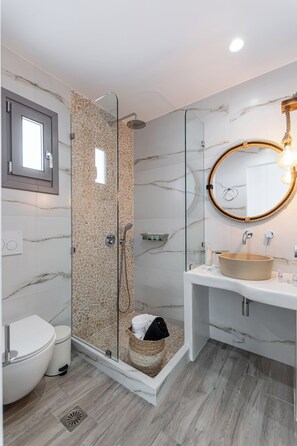 A modern bathroom with a glass-enclosed shower, a marble wall, a round mirror, and a white sink. - Naxos Contelibro (Naxos)