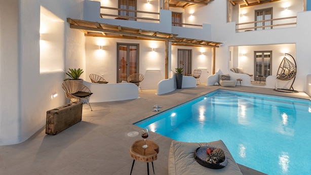 Una villa moderna con piscina, pérgolas de madera y mobiliario exterior.