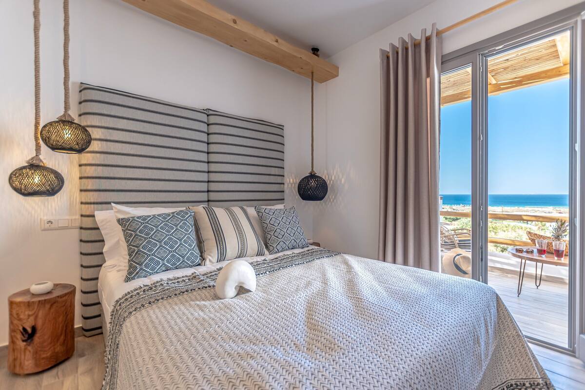A bedroom with a large bed, striped headboard, and a view of the beach.