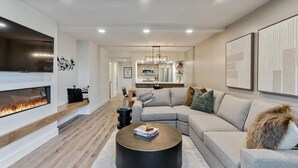 A modern living room with a fireplace, a sectional sofa, a coffee table, and a kitchen in the background.