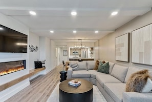 A modern living room with a fireplace, a sectional sofa, a coffee table, and a kitchen in the background.
