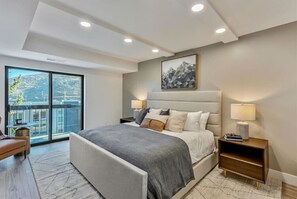 Un dormitorio moderno con una cama grande, lámparas de noche, vistas a través de un ventanal corredero y un cuadro en la pared.