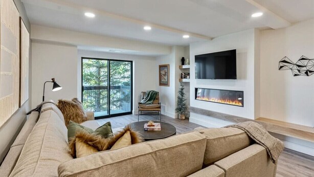 A modern living room with a sofa, a fireplace, a TV, and a large window.