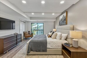 Un dormitorio moderno con una cama, lámparas de noche, un televisor, una silla y un ventanal grande.