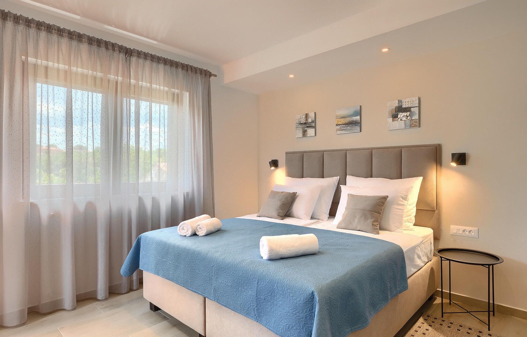 A bedroom with a bed, curtains, a bedside table, and wall art.