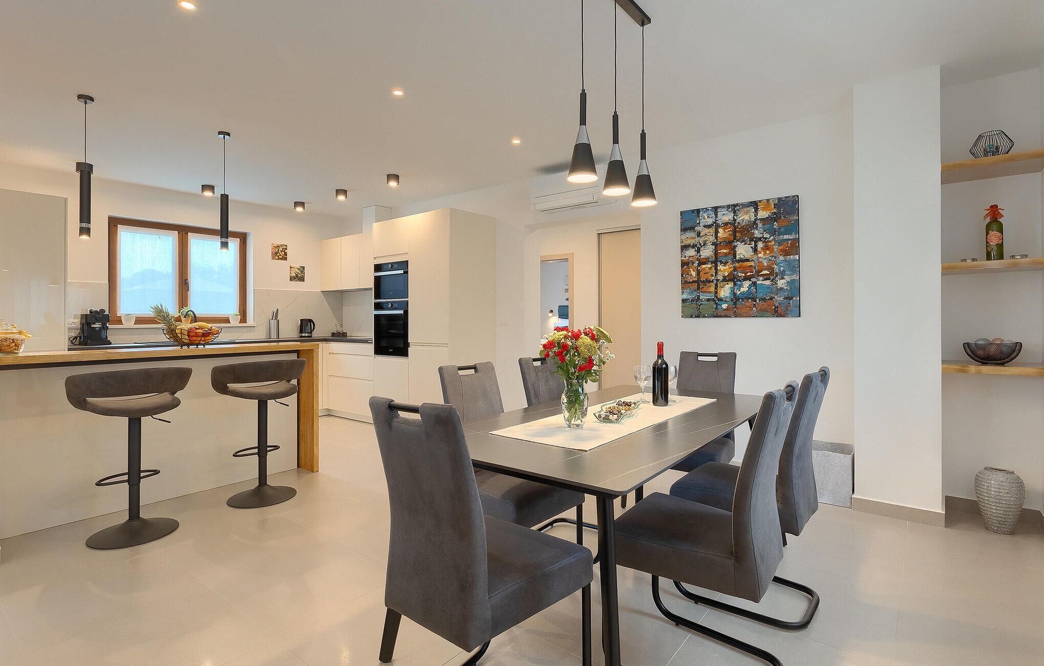 Una cocina moderna con una isla central, taburetes de bar y una mesa de comedor con sillas.
