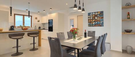 Una cocina moderna con una isla central, taburetes de bar y una mesa de comedor con sillas.