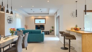 Ein modernes Wohnzimmer mit einem türkisfarbenen Sofa, einem Essbereich mit Holztisch und -stühlen sowie einer Küchenzeile mit einer Bar.