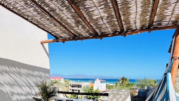 Eine Hängematte auf einem Balkon mit Blick auf die Küste, inklusive Tisch und Stühlen.