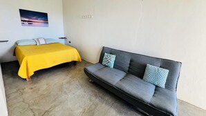 Ein Zimmer mit einem Bett, einem Schlafsofa, einer Klimaanlage, einem Deckenventilator und einem an der Wand befestigten Lichtschalter.