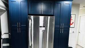 Une cuisine de taille réduite avec des meubles de couleur bleu foncé, un réfrigérateur en acier inoxydable et une porte blanche ornée d’une ancre rouge.