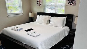 Un lit bien fait, avec du linge de lit blanc, une tête de lit en bois foncé et un tapis bleu orné de motifs d’ancres.