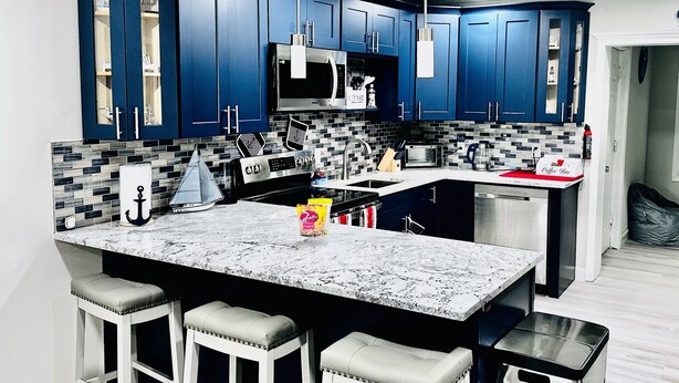 Une cuisine moderne avec des meubles bleus, un grand îlot central doté de tabourets, un four à micro-ondes et un coin café.