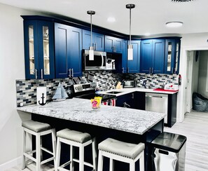Una cocina moderna con armarios azules, una isla grande con taburetes de bar, un microondas y una estación de café.