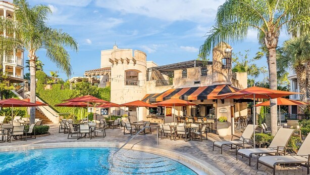 A pool area with lounge chairs and umbrellas, surrounded by palm trees and a building with a turret. - Marriott Grande Vista Spacious 1-Bedroom Villa Dec. 26, 2023 - Jan. 2, 2024. (Orlando)