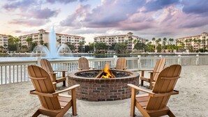 A fire pit with four Adirondack chairs, a fountain, and a view of hotel buildings across a body of water. - Marriott Grande Vista Spacious 1-Bedroom Villa Dec. 26, 2023 - Jan. 2, 2024. (Orlando)