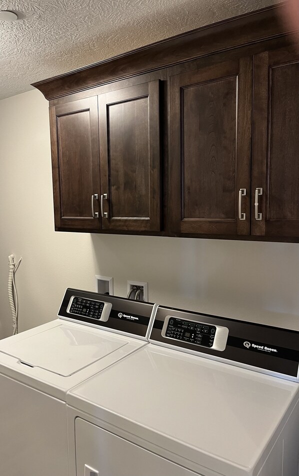 A laundry area with a front-loading washer and dryer, wooden cabinets above, and a white wall.