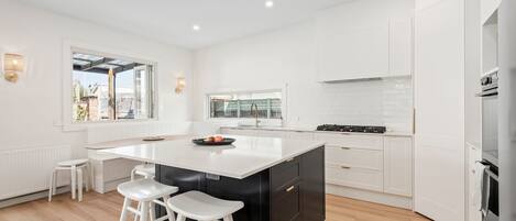 Una cocina moderna con armarios blancos, una isla central con taburetes, una ventana con vistas y una estufa de acero inoxidable.