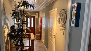 A hallway with a wooden bench, a potted plant, a door with a decorative leaf pattern, and a wall-mounted light fixture. - Headlineee (Norrbottens län)