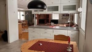 A modern kitchen with white cabinets, a wooden dining table, and a black pendant light. - Headlineee (Norrbottens län)