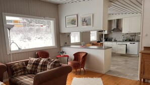 A modern kitchen with white cabinets, a central island, and a dining area with a brown sofa and plaid cushions. - Headlineee (Norrbottens län)