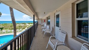 Un balcon avec des chaises blanches, une piscine et une vue sur l’océan.