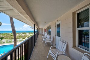 Ein Balkon mit weißen Stühlen, einem Pool und Blick auf den Ozean.