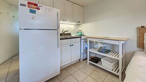 Une cuisine compacte avec des meubles blancs, un réfrigérateur, une cuisinière et une petite table dotée d’étagères.