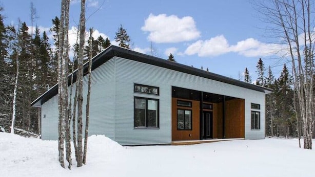 A modern, single-story building with a light blue exterior, large windows, and a wooden door.