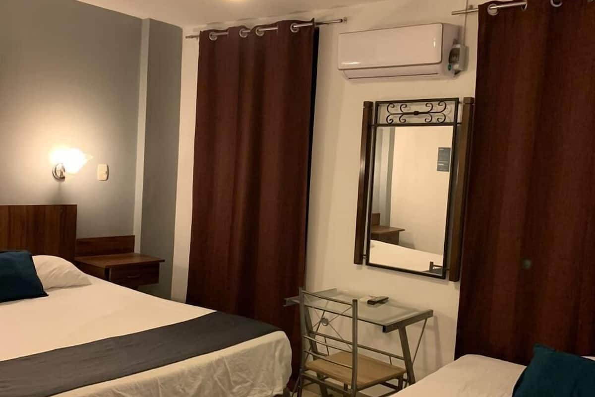 Habitación de hotel con dos camas, un ventilador de techo, una mesita, una silla y un espejo.
