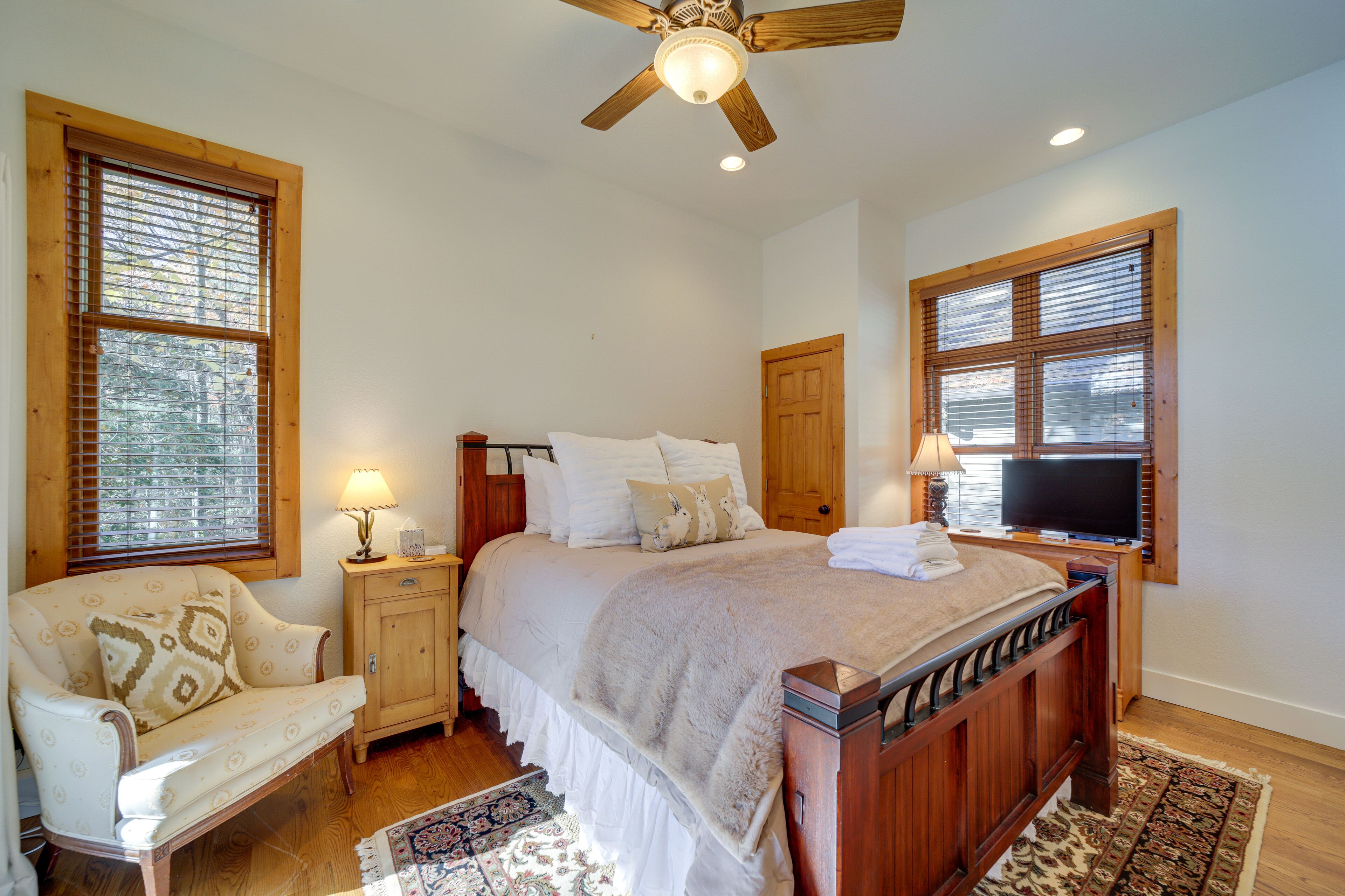 A bedroom with a wooden bed, a wooden nightstand, a chair, a television, and a ceiling fan.