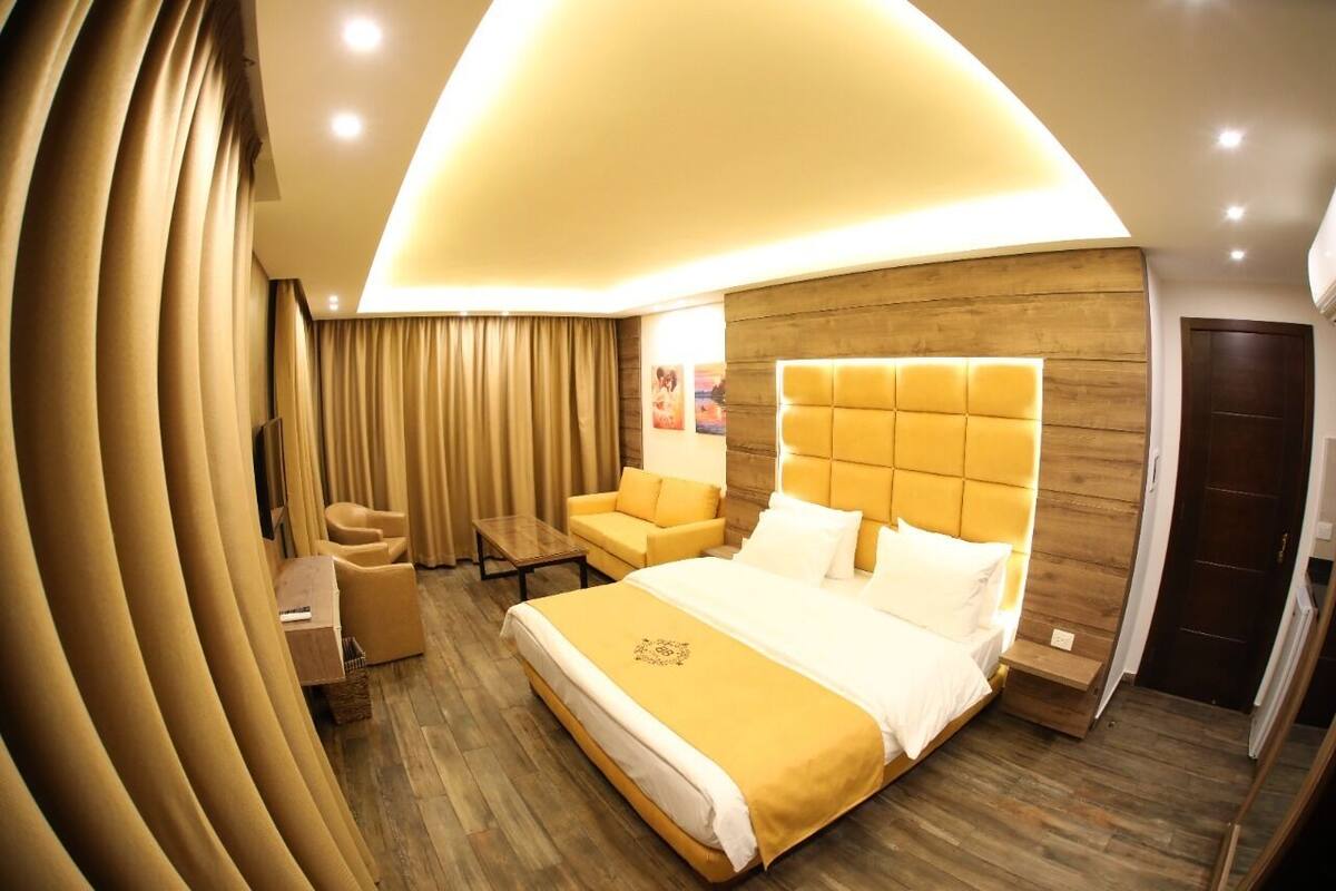 A modern hotel room with a large bed, a sofa, a small table, and a wooden accent wall.