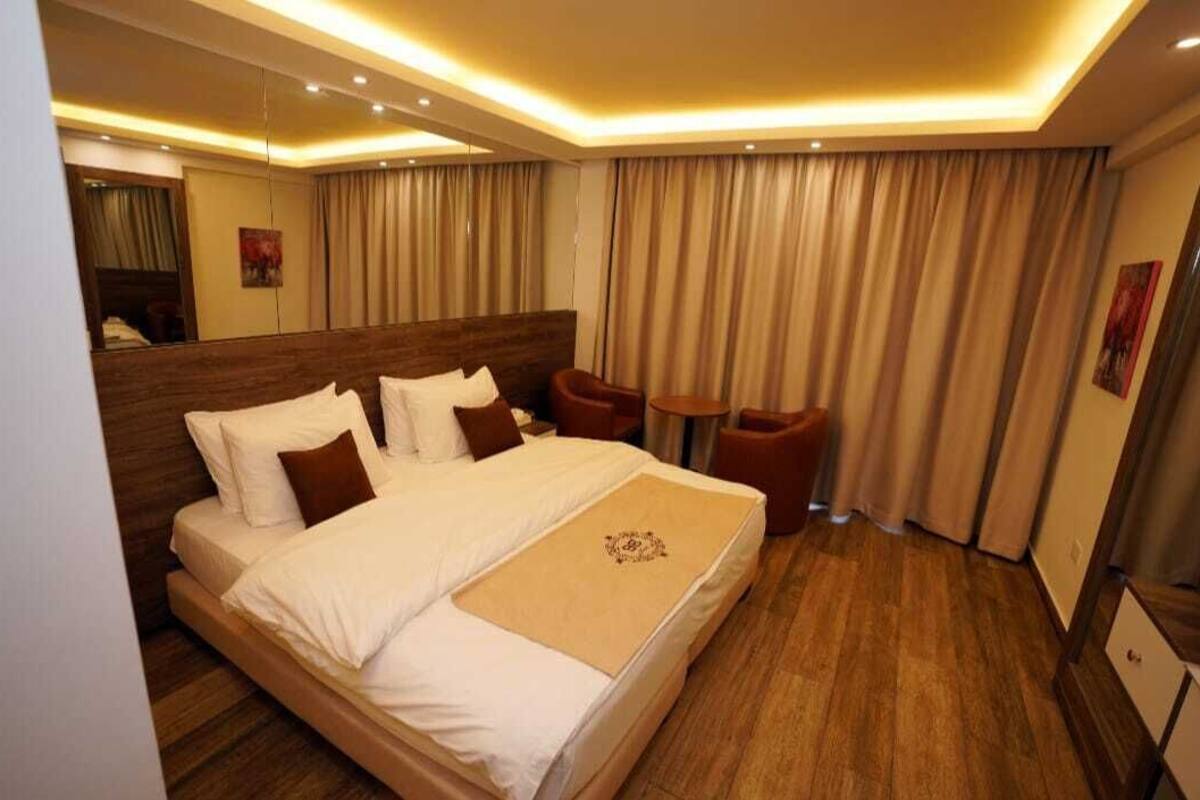 A hotel room with a large bed, a wooden headboard, a small table, and a chair.