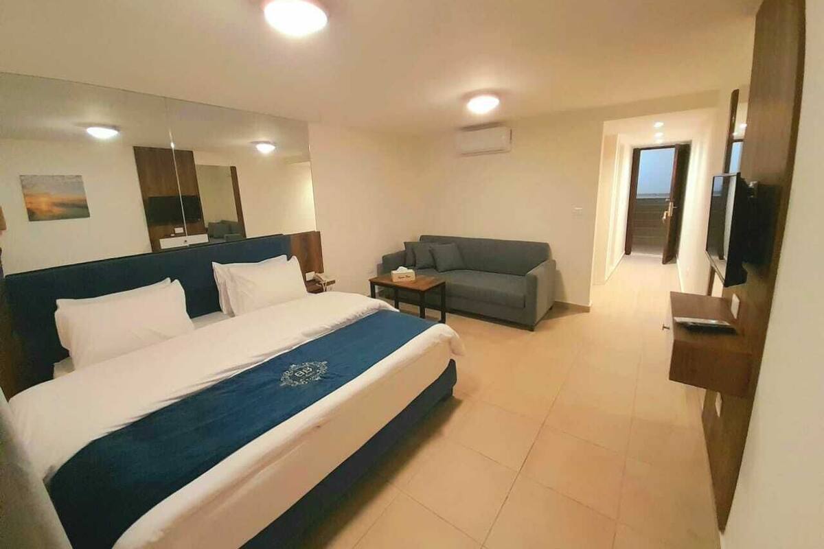 A hotel room with a large bed, a sofa, a TV, and a desk.