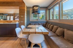A modern kitchen with wooden cabinetry, a dining area with a wooden table and white chairs, and a built-in bench with cushions.