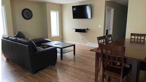 A living room with a sofa, coffee table, dining table with chairs, a flat-screen TV mounted on the wall, and a clock on the wall. - Spacious 2 Bdm close to Airport

 (Regina)