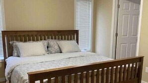 A bedroom with a wooden bed frame, a white bedspread, and a window with blinds. - Spacious 2 Bdm close to Airport

 (Regina)