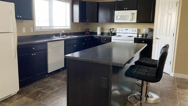 A modern kitchen with dark cabinets, a large island, a microwave, and a dishwasher. - Spacious 2 Bdm close to Airport

 (Regina)