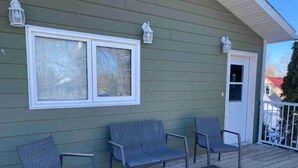 A covered porch with four chairs and a glass table, a white door, and two windows with white frames. - Spacious 2 Bdm close to Airport

 (Regina)