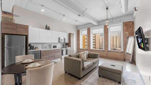 A modern kitchen with white cabinets, stainless steel appliances, and a dining area with a table and chairs. - 1BR Downtown Loft - Skyline Views & Free Breakfast (Dallas)