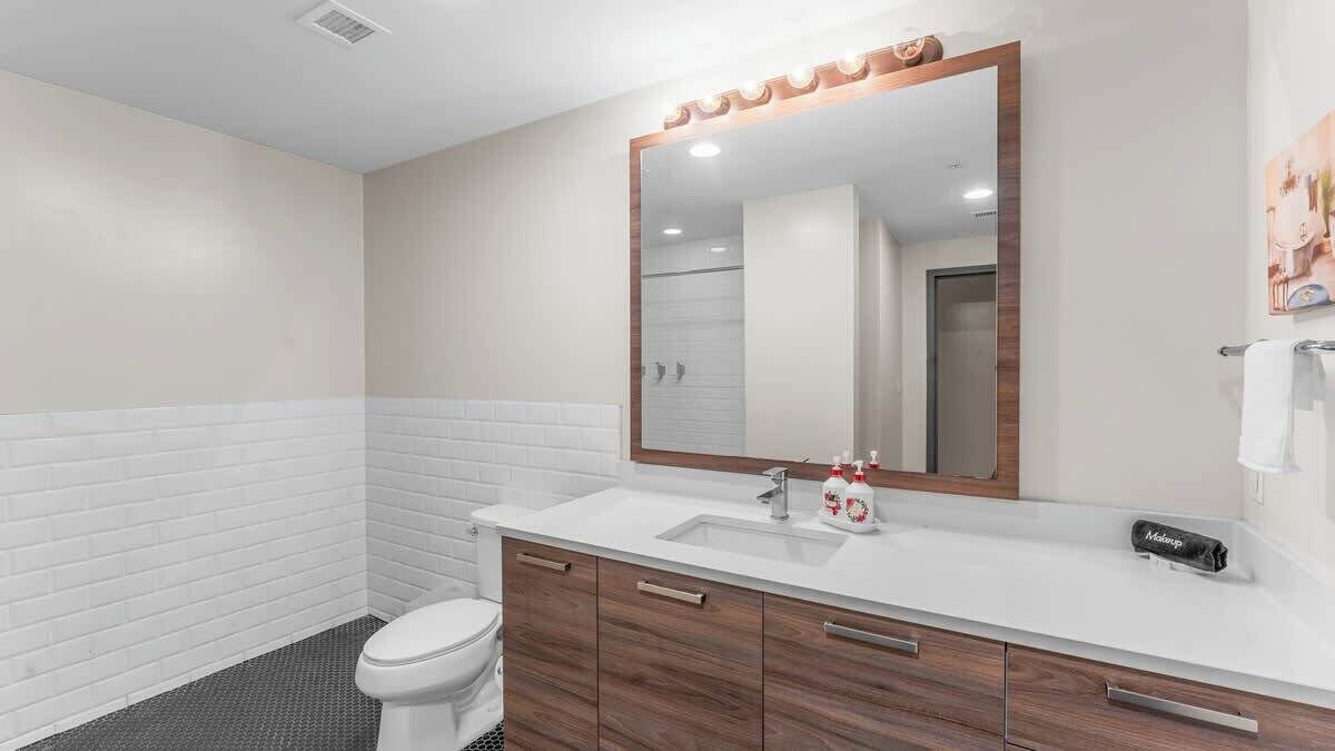 Un bagno moderno con un lavandino bianco, un mobile contenitore in legno e un ampio specchio illuminato.