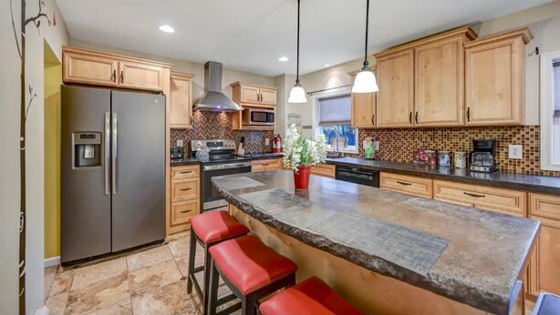 A modern kitchen with wooden cabinets, a stainless steel refrigerator, a large island with bar stools, pendant lighting, and a tiled backsplash. - Newly renovated, game room, skiing, sauna, water parks, golf, suites  (Cresco)